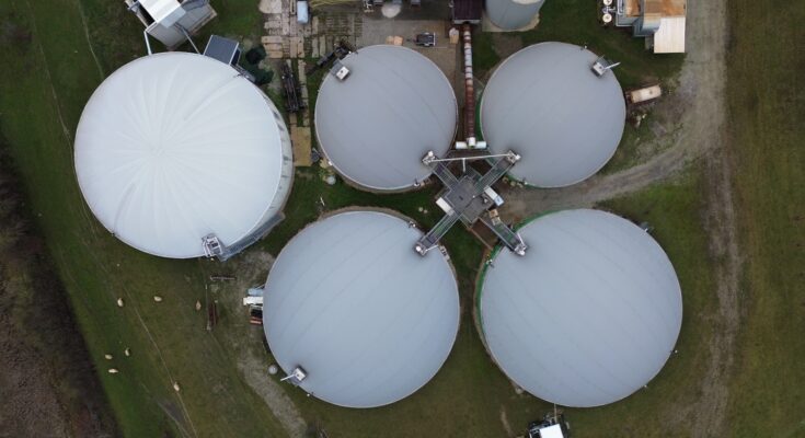 a group of large white tanks sitting on top of a lush green field. Biogas
